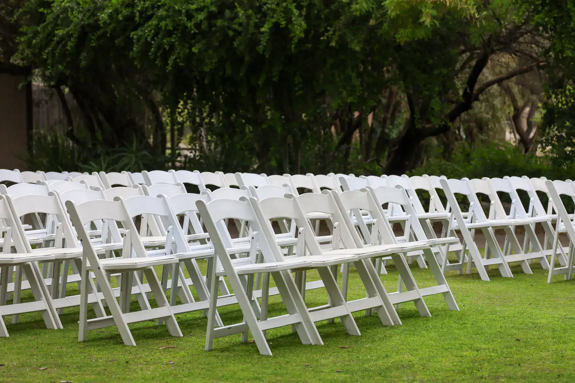Rows of empty white folding chairs are arranged outdoors on green grass, with trees and greenery in the background, suggesting a setup for an event such as a wedding or ballroom dance Suffolk County, NY.