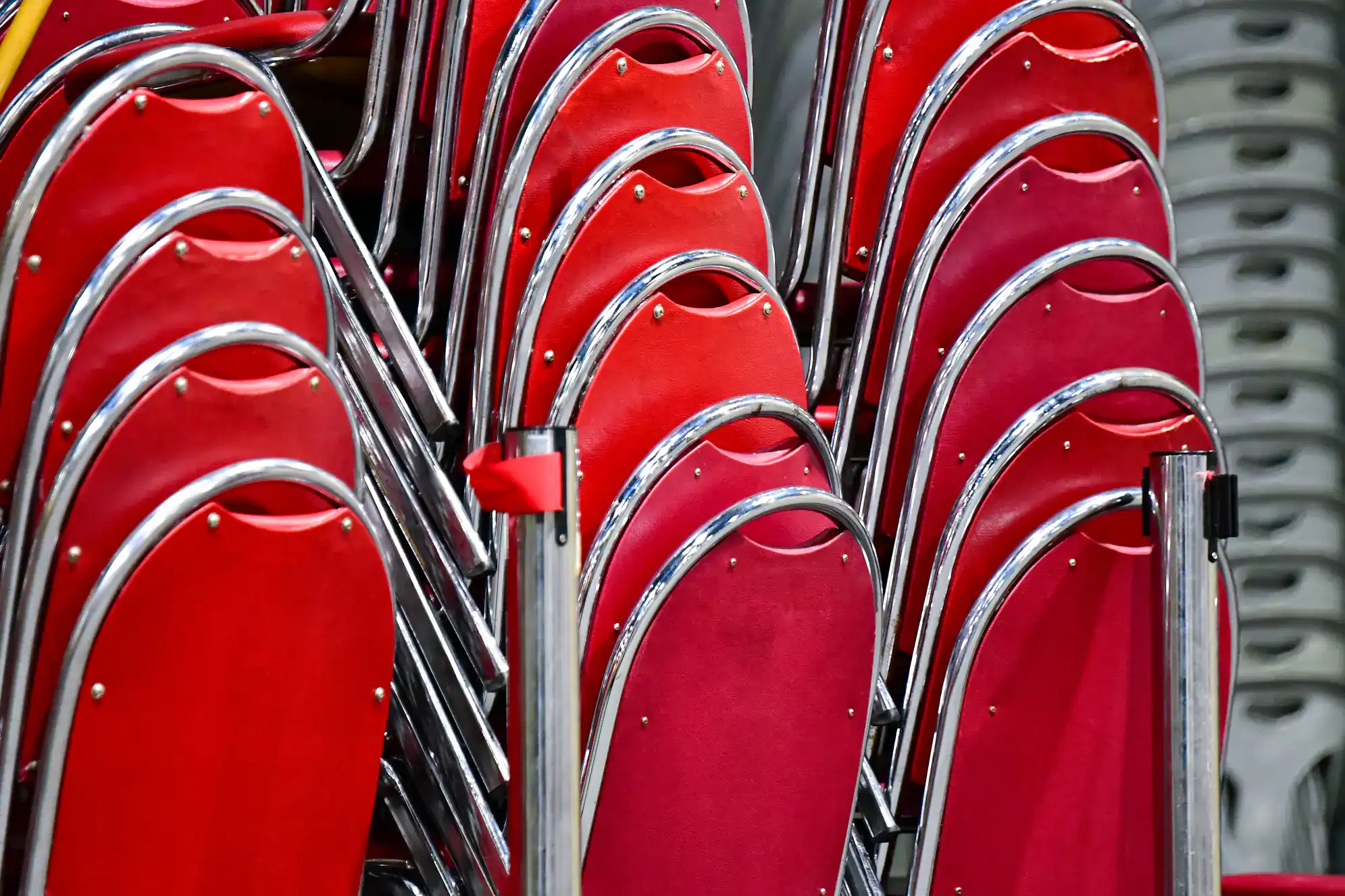 A close-up of several rows of stacked red metal chairs with shiny chrome frames, arranged neatly in an indoor setting&mdash;perfect seating for ballroom dance Suffolk County events or dance lessons in Suffolk County, NY.