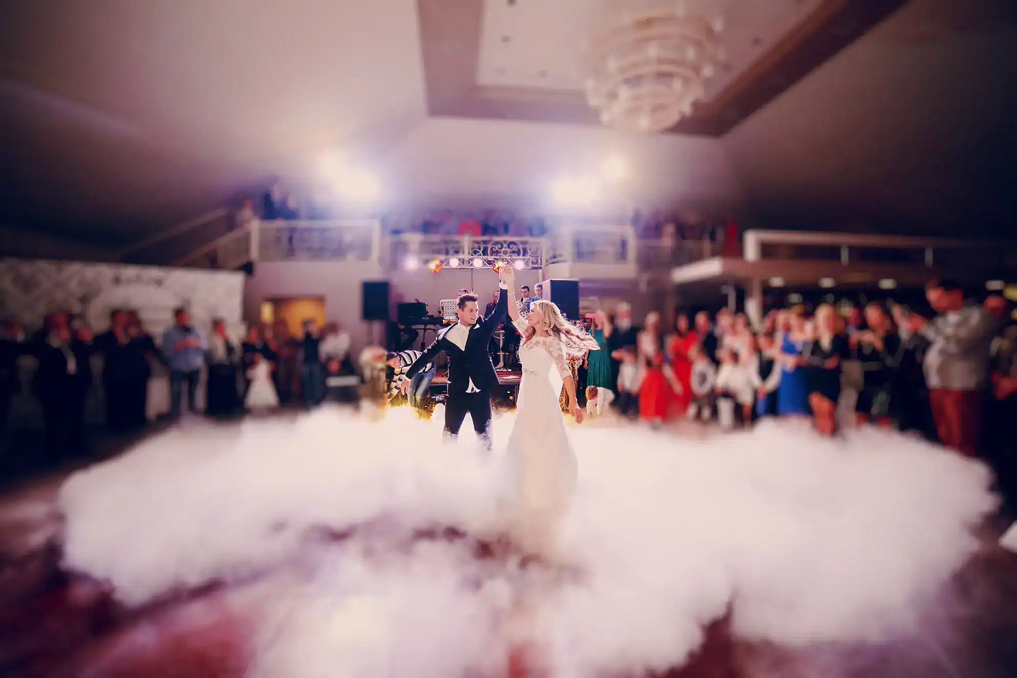 A bride and groom share a ballroom dance in Suffolk County, gliding across a cloud of white fog as guests look on, with bright lights overhead creating a dreamy NY atmosphere.